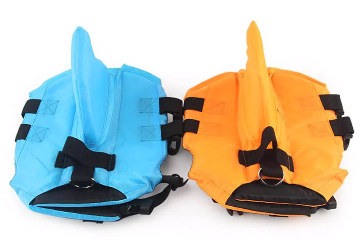 Dog life jacket with shark fin, offering buoyancy and fun for all water activities; bright material, adjustable straps.