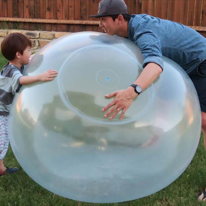A child joyfully playing with a giant inflatable water bubble ball toy in a sunny park.
