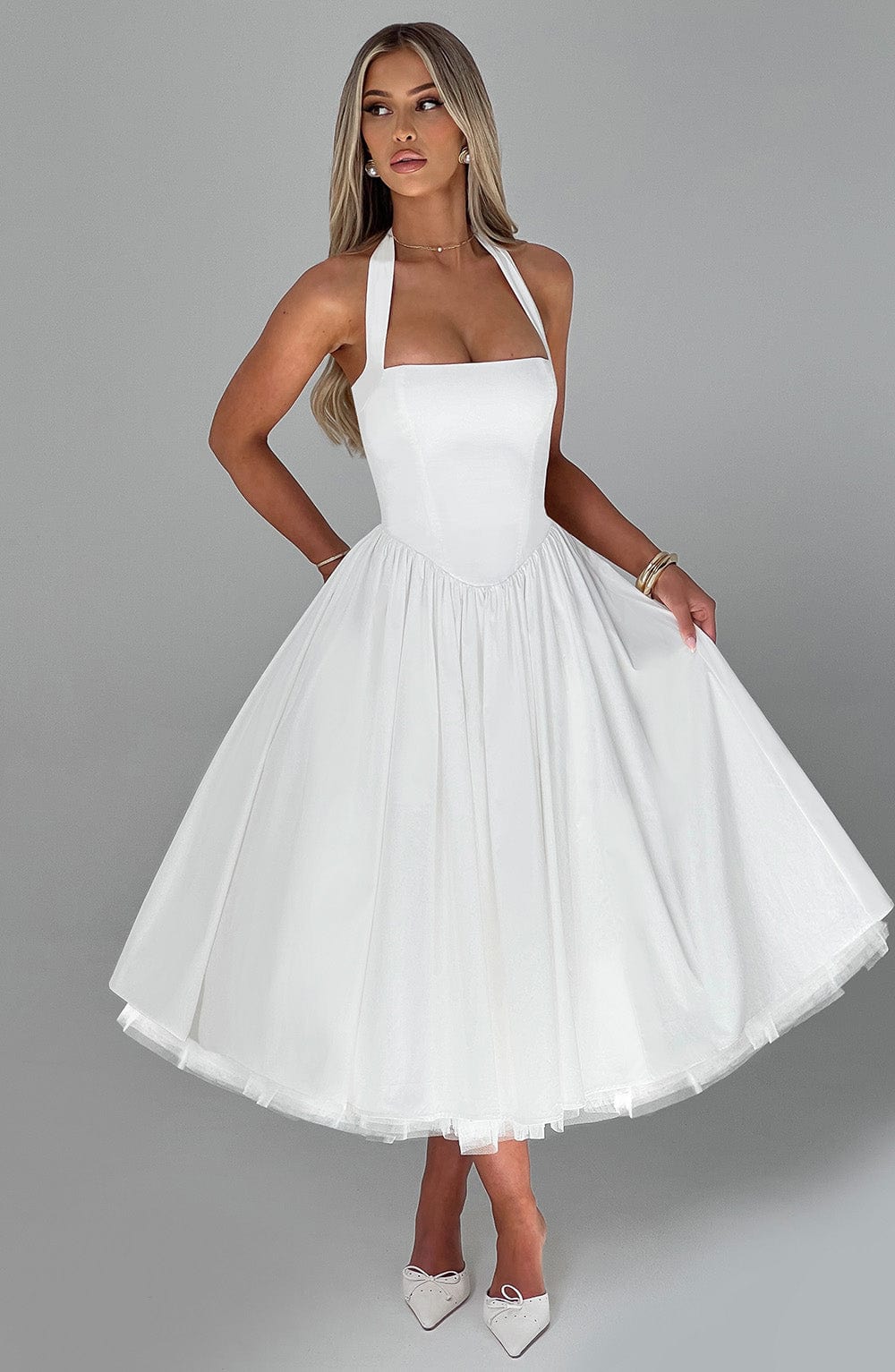 Woman posing confidently in a white halter neck midi dress, ideal for wedding guests & formal events