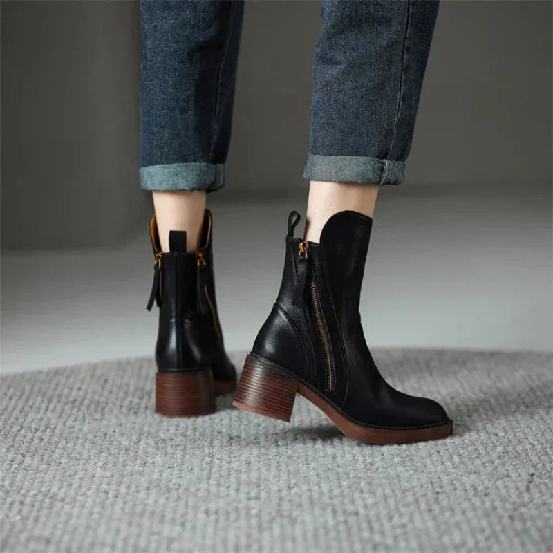 Close-up of a women's black ankle boot, showcasing the sturdy block heel and functional zipper detail.