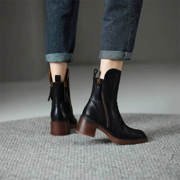 Close-up of a women's black ankle boot, showcasing the sturdy block heel and functional zipper detail.