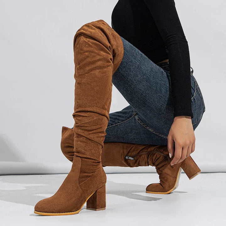 Woman wearing black over-the-knee heeled boots, styled with a dress for an elegant look