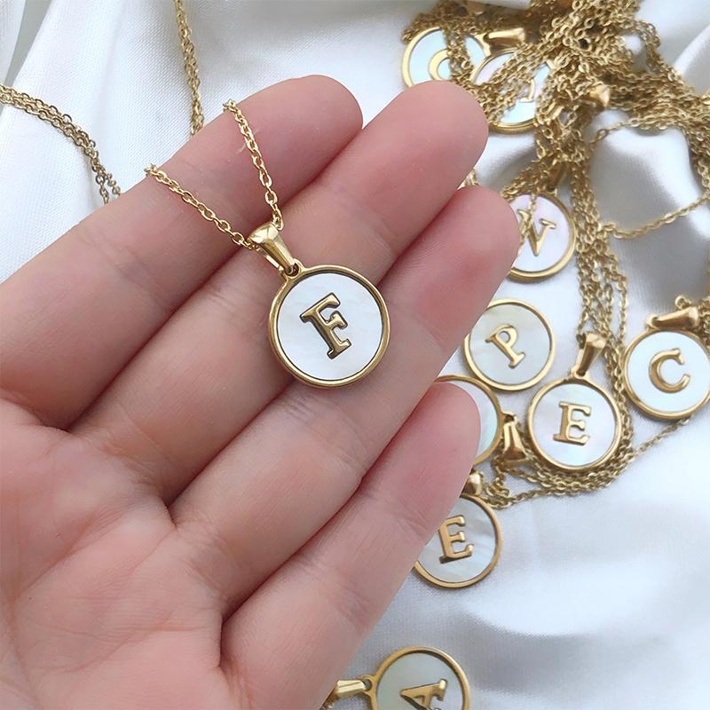 Close-up of a women's round shell initial necklace, 'S' engraved, gold-plated stainless steel, fashion accessory