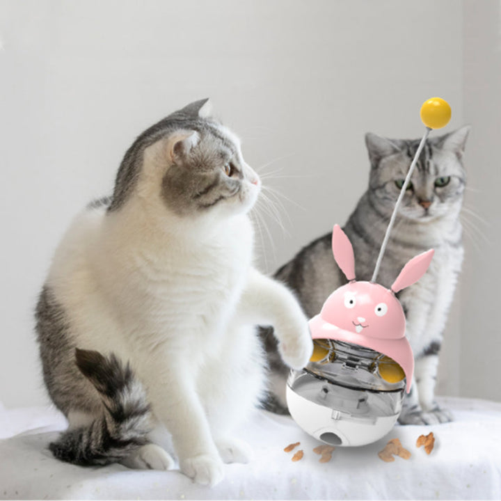 Cat enrichment toy, tumbler design, with a playful cat batting at the dispenser