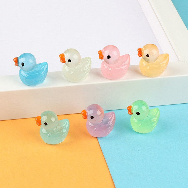 Several luminous mini duck figurines scattered in a miniature garden, glowing softly at dusk.