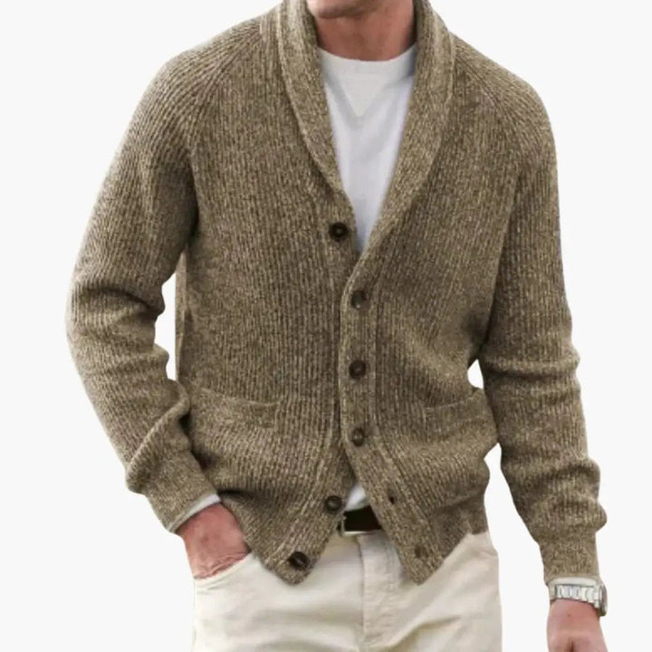 Full view of a man wearing a dark blue shawl collar cardigan sweater, a smart layering piece.
