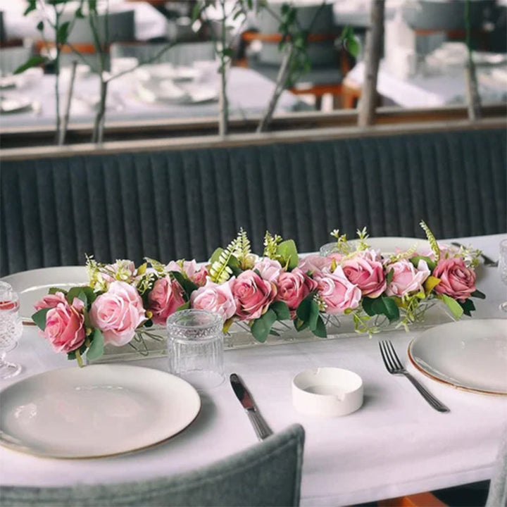 Wedding centerpiece featuring a clear acrylic flower vase brimming with white roses and greenery.