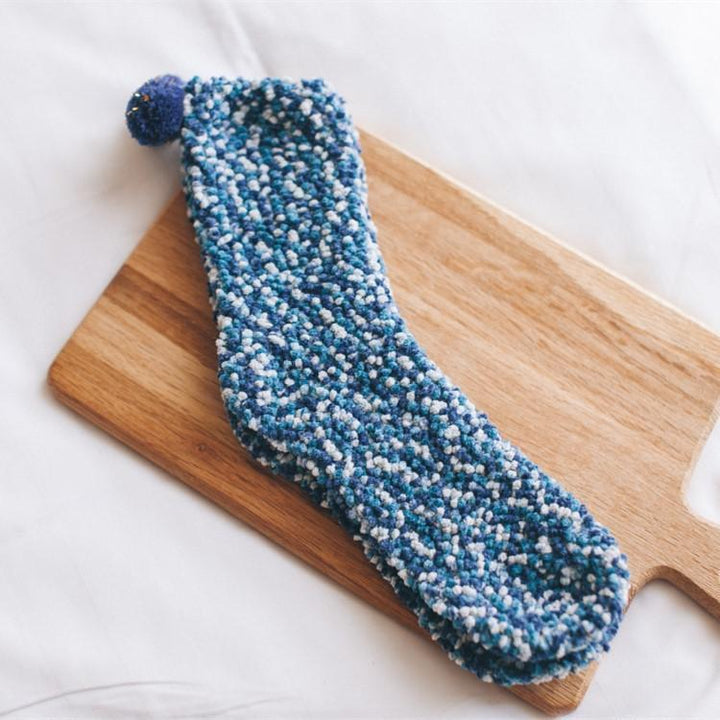 Lifestyle image of women's fluffy cupcake slipper socks on a wooden floor next to a warm cup.