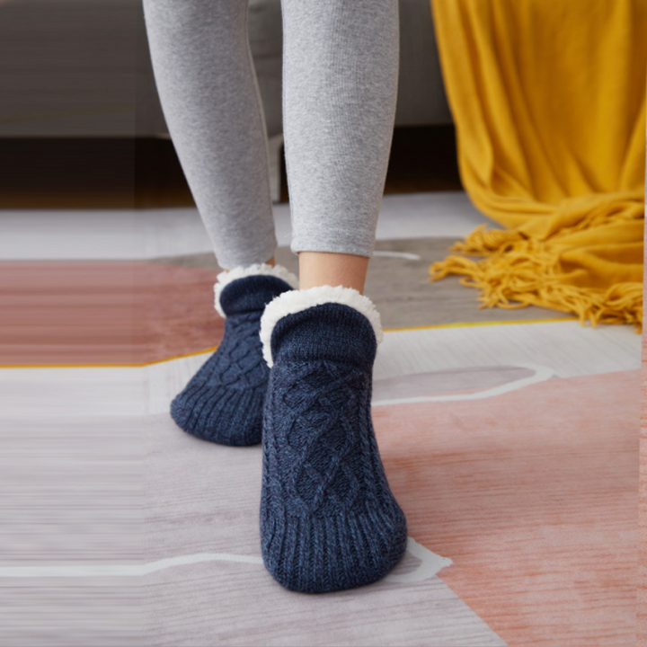 Side view of a warm grey unisex slipper sock on a wooden floor, illustrating its thick, soft design.