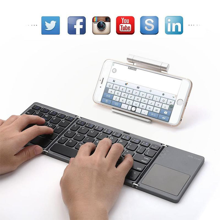 Portable electronics accessory: a tri-fold wireless keyboard with touchpad next to a laptop
