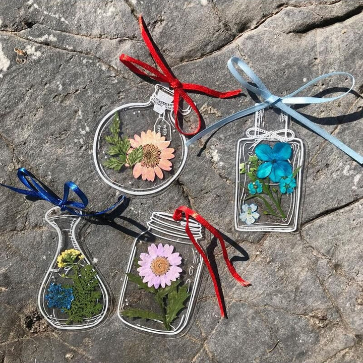 Closeup of a handmade transparent bookmark featuring a delicate purple dried flower and green foliage.