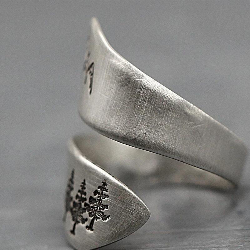 Close-up of a silver adjustable ring with intricate dandelion and mountain engravings