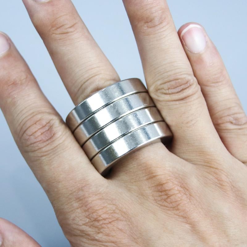 A hand demonstrates the folding action of the metallic four-finger stress relief fidget ring.