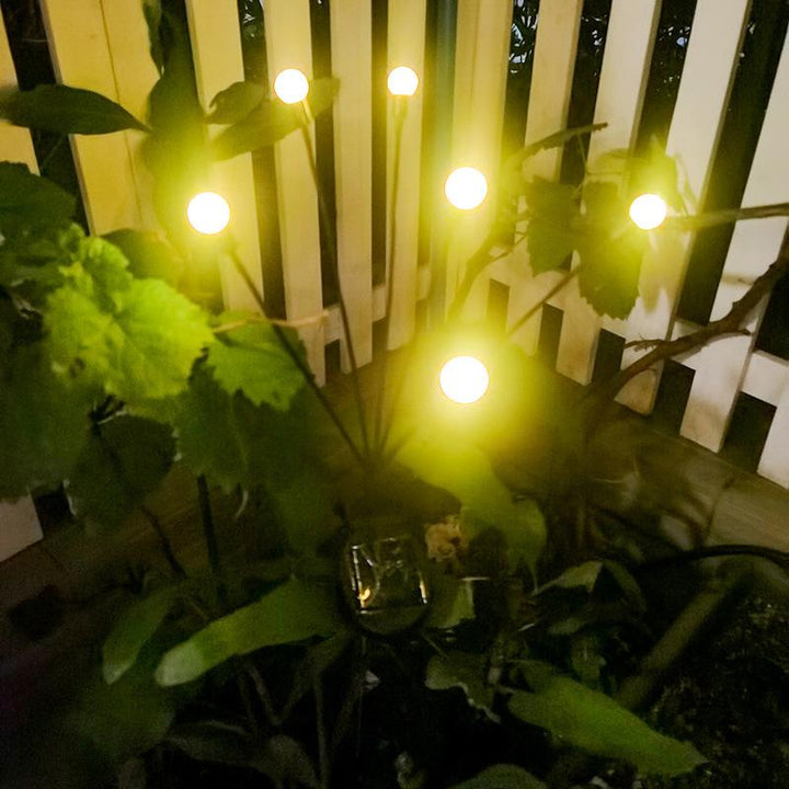 Close-up of a solar LED firefly light with its warm glow illuminating a garden path