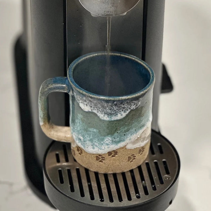 Handmade ceramic coffee mug with an ocean-inspired finish and subtle paw print detail, kitchenware item