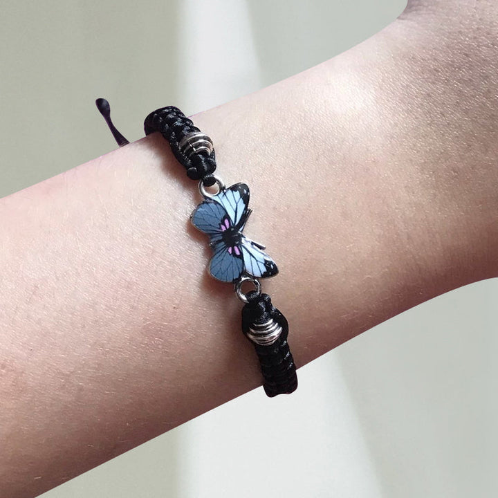 Close-up of the silver butterfly charm on a black adjustable woven friendship bracelet.