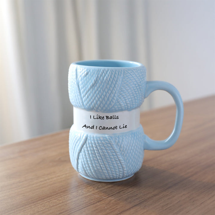 Product shot of a unisex ceramic mug with a playful knitting yarn ball, a must-have for crafters.