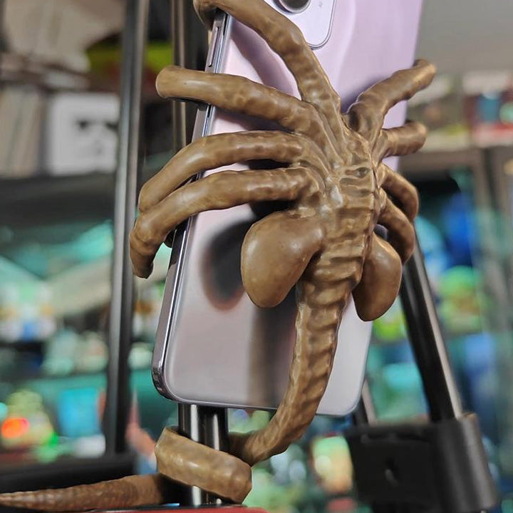 Horrible Creature Phone Stand on a desk holding a smartphone, a cool sci-fi gift idea.
