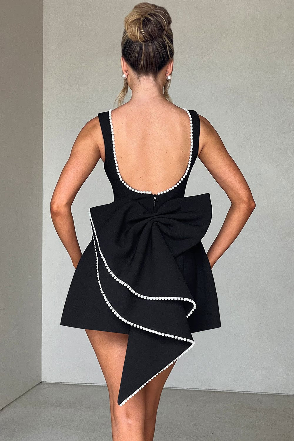Party-ready women's backless A-line mini dress, featuring intricate pearl trim and an eye-catching statement bow.