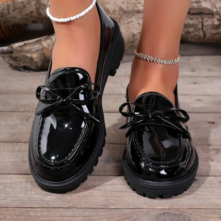 Detail shot of the penny strap on women's glossy patent loafers, quality craftsmanship