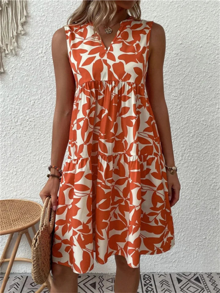 Close-up: vibrant green leaf print on a women's V-neck mini dress. Soft fabric, tiered design. Effortless summer style.