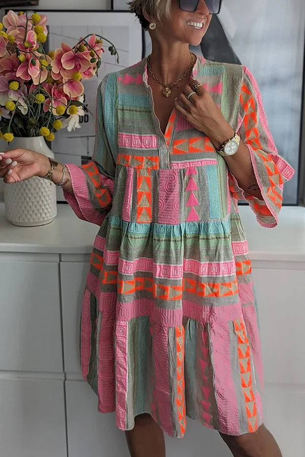 Casual women's pink spring day dress, a tiered mini with a V-neck, 3/4 sleeves, and geometric pattern.