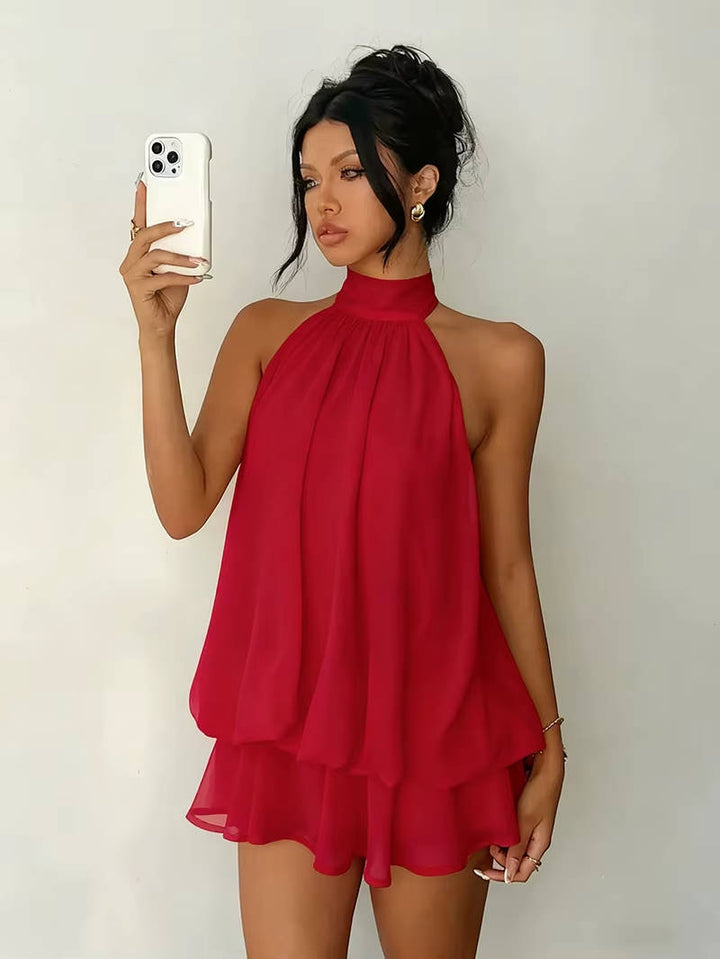 Side profile of a women's elegant halter mini dress, sleeveless, with beautiful drape, ruffle hem, and open back.