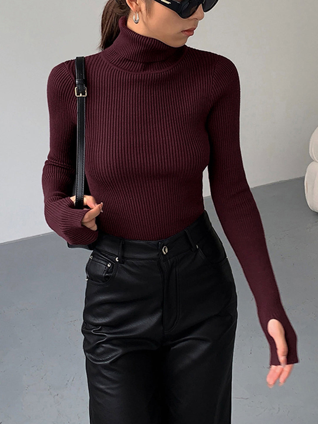 Model wearing a form-fitting black ribbed turtleneck sweater, highlighting its flattering silhouette.