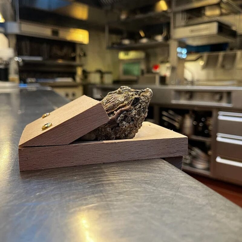 Top-down view of a wooden oyster shucking clamp on a kitchen countertop, seafood tool