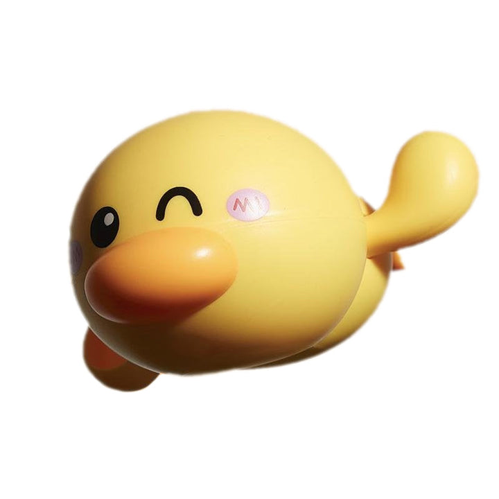 A child laughing while playing with a yellow wind-up swimming duck bath toy in the tub